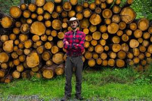 ritratto di boscaiolo nella foresta, molti grandi tronchi di pino sullo sfondo. giovane escursionista maschio in posa vicino alla farina di sega nella foresta di pini. foto