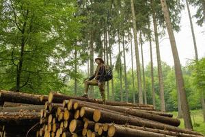 giovane escursionista femminile in posa vicino alla farina di sega nella foresta di pini. molti tronchi d'albero nella foresta. viaggiatore zaino in spalla donna. foto