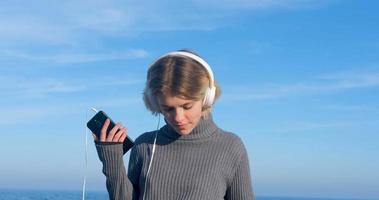 la giovane donna bella ascolta la musica con le cuffie all'aperto sulla spiaggia contro il cielo blu soleggiato foto