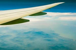 ala dell'aereo sopra la montagna. aereo che vola su cielo blu e nuvole bianche. vista panoramica dalla finestra dell'aeroplano. volo di una compagnia aerea commerciale. ala dell'aereo. concetto di meccanica di volo. volo internazionale. foto