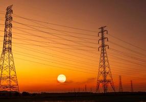 traliccio elettrico ad alta tensione e filo elettrico con cielo al tramonto. pali elettrici. concetto di potenza ed energia. torre di griglia ad alta tensione con cavo metallico. bellissimo grande sole al tramonto con cielo rosso-arancione. foto