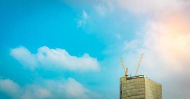 gru da costruzione su un grattacielo con cielo blu e nuvole bianche. cantiere di edificio commerciale o condominio o appartamento in città. affari immobiliari. sfondo di architettura foto