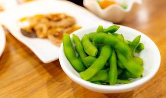 edamame o semi di soia verdi sbollentati in una ciotola bianca su un tavolo di legno al ristorante giapponese. baccelli di fagioli di soia verdi su cibo giapponese sfocato. cibo ricco di fibre e proteine. proteine vegetali. dieta vegana. foto