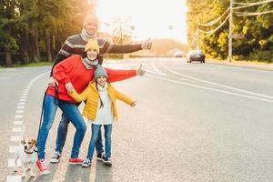 il ritratto della madre di famiglia, del padre e della figlia piccola camminano con l'animale domestico, stanno sulla strada, alzano i pollici come segno di ok, esprimono approvazione o accordo, sono di buon umore dopo aver trascorso del tempo all'aria aperta foto