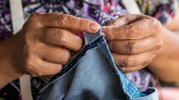 mani e dita di donne anziane che riparano denim. foto