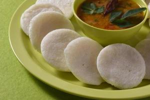 idli con sambar in una ciotola su sfondo verde, piatto indiano cibo preferito dell'India meridionale rava idli o semolino pigramente o rava pigramente, servito con sambar e chutney di cocco verde. foto