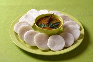 idli con sambar in una ciotola su sfondo verde, piatto indiano cibo preferito dell'India meridionale rava idli o semolino pigramente o rava pigramente, servito con sambar e chutney di cocco verde. foto