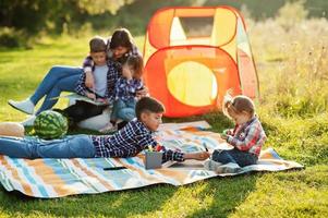 famiglia che trascorre del tempo insieme. madre con quattro bambini all'aperto in coperta da picnic e tenda per bambini. foto