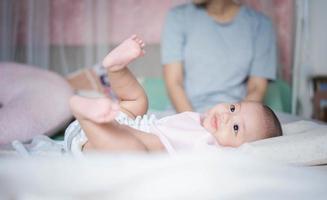 famiglia felice, carino asiatico neonato sdraiato giocare sul letto guardando qualcosa. mentre tua madre si prende cura con amore nelle vicinanze. ragazzino innocente il primo giorno della sua vita. concetto di festa della mamma. foto