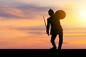 silhouette di uomo d'affari in costume da cavaliere spada e scudo con tracciato di ritaglio sfondo tramonto, combattendo il concetto di guerriero d'affari. foto