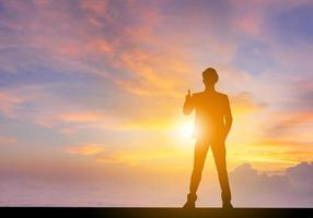 silhouette di uomo di ingegnere aziendale che dà il pollice in su come segno di successo al tramonto sullo sfondo del cielo di sera. foto