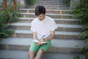il giovane outddur nel parco scrive su un taccuino, uno studente o uno scrittore al lavoro foto
