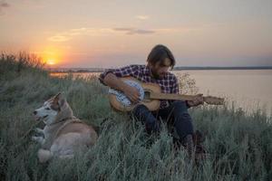 chitarrista folk o country nella foresta con cane, uomo nei boschi, falò e sfondo del tramonto foto