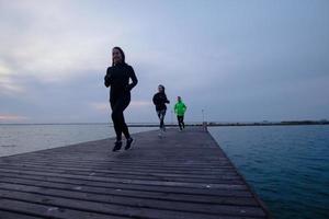 gruppo di giovani che si allenano all'aperto, esercizi di corridori, sfondo di mare o fiume foto