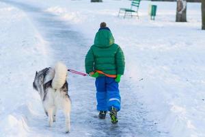 ragazzo felice gioca con il cane husky nel parco invernale pieno di neve foto