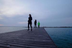 gruppo di giovani che si allenano all'aperto, esercizi di corridori, sfondo di mare o fiume foto