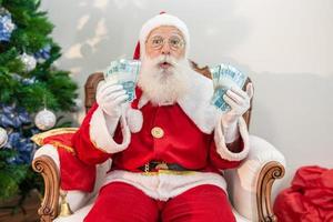 babbo natale che conta banconote brasiliane. note reali. Banconote da 100 reais. concetto di risparmio per la fine dell'anno. spesa durante il natale. speso in regali di natale. foto