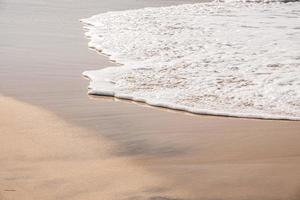 onde morbide con schiuma dell'oceano sullo sfondo della spiaggia sabbiosa foto