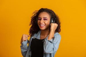 concetto di persone, musica, emozioni. felice donna spensierata con acconciatura afro balla al ritmo della melodia, chiude gli occhi ascolta una canzone ad alto volume in cuffia. bella donna afro con le sue cuffie foto