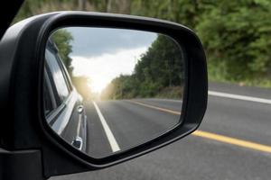 vista interna dell'ala degli specchi. vista posteriore di un'auto grigia con strada asfaltata e alberi verdi durante il giorno. libero traffico nelle zone rurali. foto