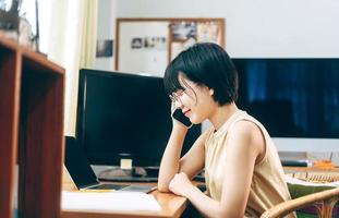 la giovane donna asiatica adulta rimane e lavora dall'ufficio a casa utilizzando lo smartphone al coperto il giorno. foto