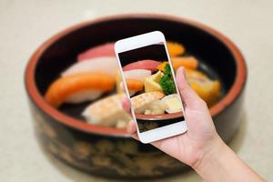 mano femminile che scatta foto del set di sushi con il telefono cellulare