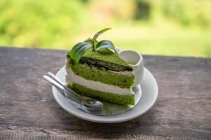 Torta al tè verde biologico con panna montata e foglia di tè in un piatto bianco su barra di legno foto