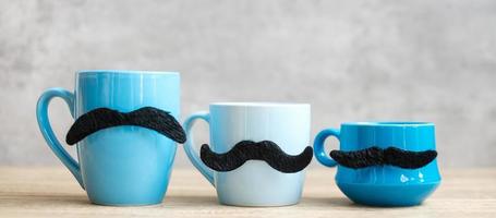 tazza di caffè blu e tazza da tè con decorazioni di baffi neri su sfondo tavolo in legno al mattino. novembre blu, felice festa del papà e concetto di giornata internazionale degli uomini foto