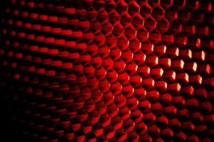 struttura della griglia a nido d'ape del primo piano con luce rossa. sfondo astratto con motivo a forma esagonale in metallo rosso e scuro. equipaggiamento modificatore di luce. nido d'ape in metallo. modello futuristico. rete di celle a griglia di miele. foto