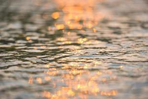 luce solare astratta riflettente sullo sfondo dell'acqua, luci bokeh sulla superficie dell'acqua al tramonto natura estate o primavera oceano mare foto