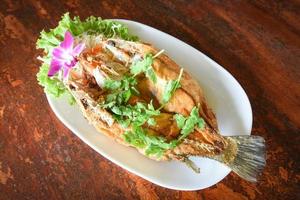 pesce fritto con erbe e verdure, cibo cotto filetto di pesce branzino su piatto su tavola di legno foto