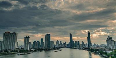 paesaggio urbano di un edificio moderno vicino al fiume al mattino con cielo arancione all'alba e nuvole a bangkok in tailandia. edificio per uffici di architettura moderna. grattacielo con cielo mattutino e ruota panoramica. foto