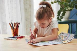 studente diligente. la bambina carina della scuola d'arte disegna i suoi primi dipinti con matite e pennarelli foto