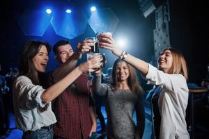 bevilo fino in fondo. gruppo di giovani amici che sorridono e fanno un brindisi in discoteca foto