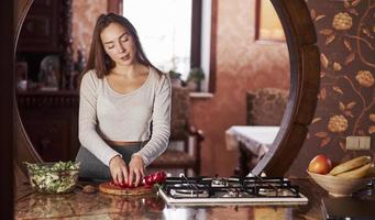 fare l'insalata preferita. bella giovane donna in piedi nella cucina moderna vicino al fornello a gas e preparare il cibo foto