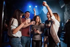 atmosfera di festa. persone felici che ballano nel night club di lusso insieme a diversi drink nelle loro mani foto