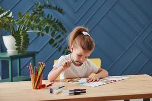 pensa a cosa aggiungere la bambina carina della scuola d'arte disegna i suoi primi dipinti con matite e pennarelli foto