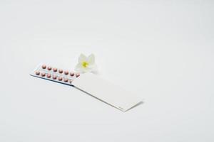 pillole anticoncezionali o pillola contraccettiva con custodia di carta e fiore bianco su sfondo bianco. concetto di pianificazione familiare. terapia ormonale sostitutiva. trattamento dell'acne ormonale con pillola anti-androgena. foto