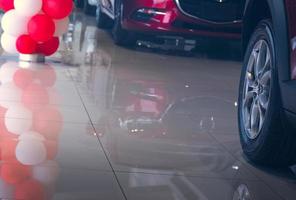 messa a fuoco selettiva su ruote e pneumatici della nuova auto rossa parcheggiata in uno showroom moderno con riflessione sul pavimento piastrellato e palloncini. concetto di concessionaria auto. promozione delle vendite in showroom. crisi del settore automobilistico. foto