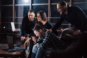 guardando una specie di film comico dopo il lavoro. team di giovani imprenditori lavora al loro progetto di notte in ufficio foto