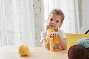 tempo per il resto. il bambino sta lavorando a maglia a casa. la bambina sveglia che si siede vicino al tavolo di legno sta imparando alcune cose nuove foto