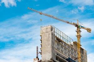 cantiere con gru e costruzione. settore immobiliare. la gru usa l'attrezzatura per il sollevamento della bobina in cantiere. edificio in acciaio e cemento. lavoro della gru contro il cielo blu e la nuvola bianca foto