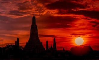 wat arun ratchawararam al tramonto con un bel cielo rosso e arancione e nuvole. il tempio buddista di wat arun è il punto di riferimento a bangkok, in tailandia. attrazione art. sagoma cielo drammatico e tempio. foto