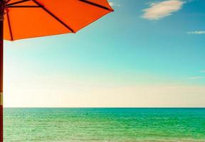 ombrellone arancione sulla spiaggia di sabbia dorata in riva al mare con acqua di mare verde smeraldo e cielo blu e nuvole bianche. vacanze estive sul concetto di spiaggia paradiso tropicale. skyline tra mare e cielo. foto