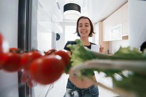 all'interno del frigorifero. ragazza carina aprire la porta e guardare cosa c'è dentro foto