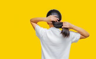 vista posteriore della donna asiatica che tiene i capelli danneggiati su sfondo giallo con spazio di copia. problema dei capelli con doppie punte nella donna. i capelli lunghi neri secchi e fragili hanno bisogno di shampoo e balsamo per il trattamento termale. foto