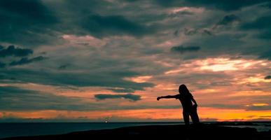 silhouette donna allenamento al mattino sulla spiaggia di pietra con bellissimo cielo all'alba. corridore donna in forma che allunga il corpo prima di correre. esercizio cardio per uno stile di vita sano. allenamento ragazza attiva da solo. foto