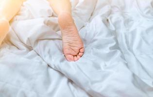 primo piano donna a piedi nudi sul letto sopra coperta bianca e lenzuolo nella camera da letto di casa o in hotel. dormire e rilassarsi concetto. mattina pigra. a piedi nudi di donna sdraiata su letto comfort bianco e piumone. foto