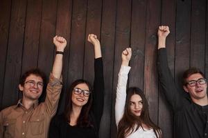 sono tutti felici. celebrare il successo. gli amici alzano le mani contro il muro di legno nero foto