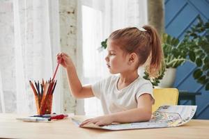 raccogliendo una matita rosa. la bambina carina della scuola d'arte disegna i suoi primi dipinti foto